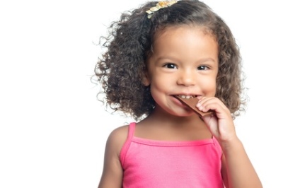 Joyful little girl with an afro hairstyle eating a chocolate bar